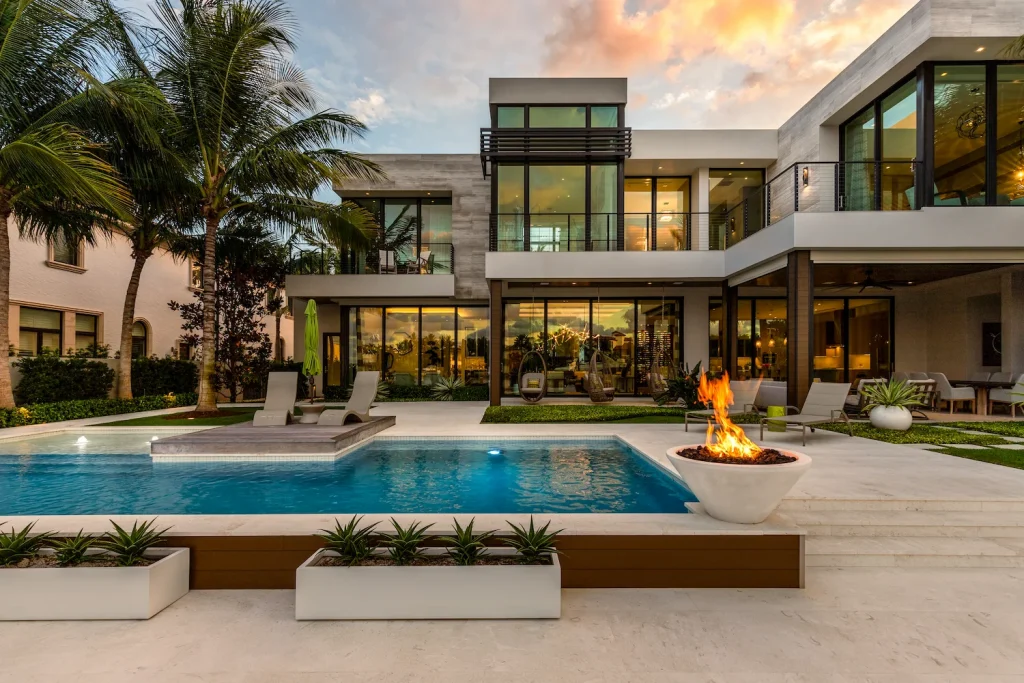 Modern two-story house with a pool, a fire bowl, palm trees and planters at dusk