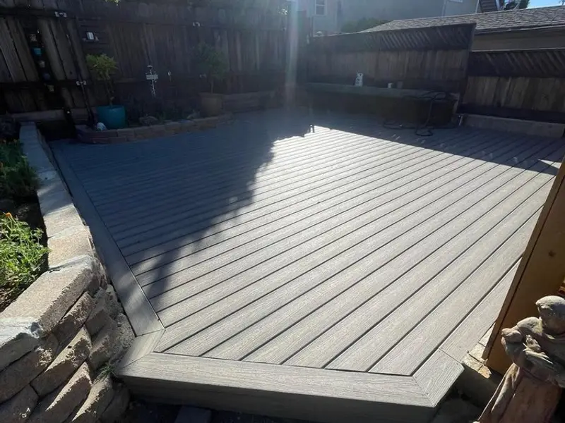 Gray composite deck with a picture-frame border next to a stacked stone planter wall