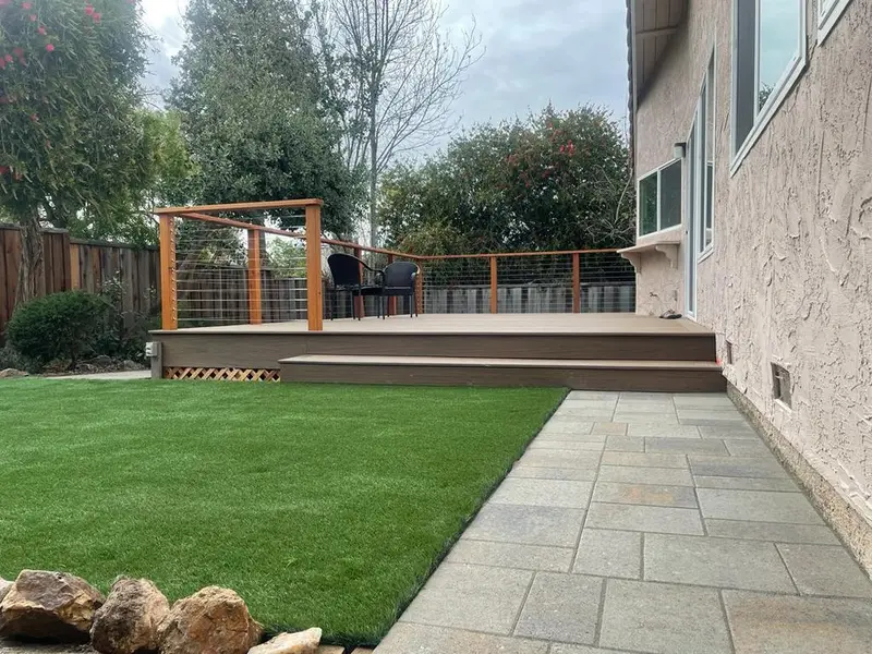 Low composite deck with a cable railing section, steps down to artificial turf and a stone walkway