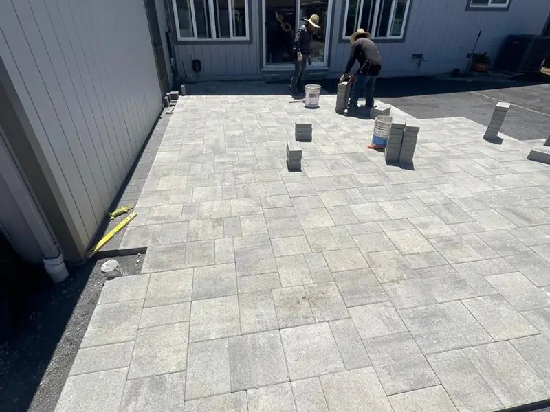 Gray paver patio being laid beside a house, with a worker setting pavers