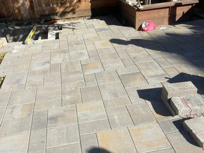 Paver patio and steps next to a raised wood planter, with pavers stacked for installation