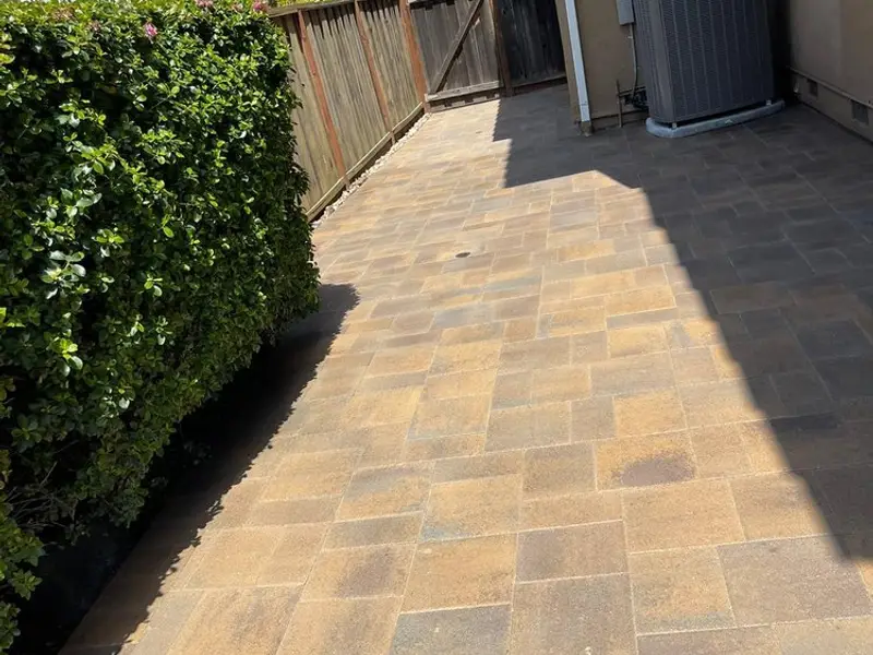 Warm-toned paver walkway running along a hedge in a side yard beside an AC unit