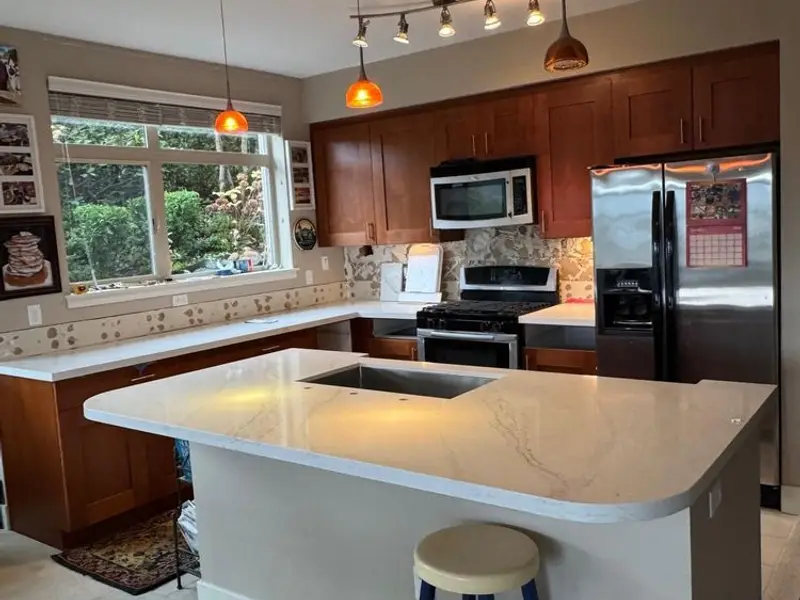Kitchen with cherry wood cabinets and a white stone island under pendant lights