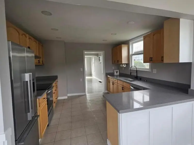 Kitchen with gray countertops, white and wood cabinets and a stainless refrigerator