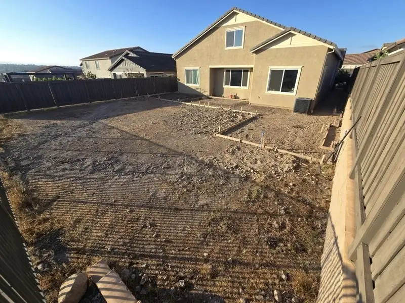 Bare backyard dirt before grading, beside a two-story house and a block wall