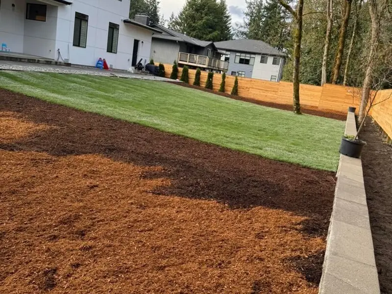 Yard with fresh bark mulch beside new lawn and a low block border